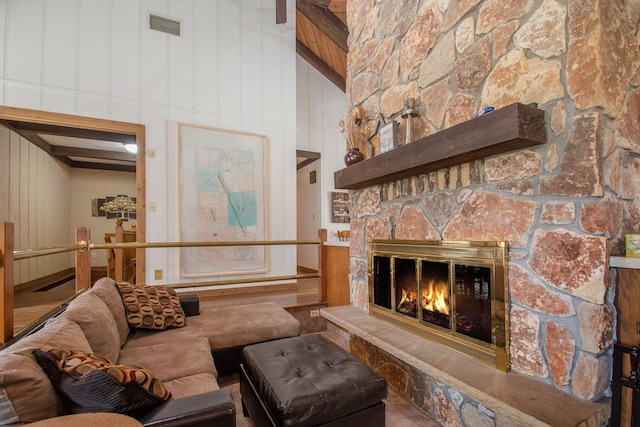 living room featuring visible vents, a high ceiling, wooden walls, a stone fireplace, and beamed ceiling
