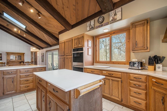 kitchen with lofted ceiling with beams, light countertops, stainless steel double oven, and a center island