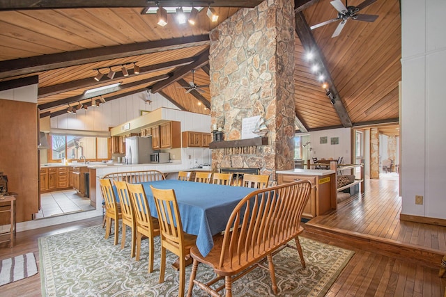 dining space with light wood-style floors, beam ceiling, a fireplace, and ceiling fan