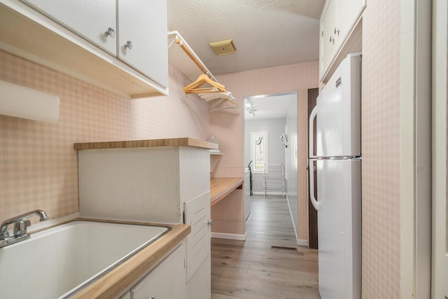 interior space featuring open shelves, freestanding refrigerator, white cabinets, a sink, and wallpapered walls