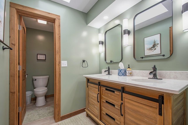 bathroom featuring baseboards, a sink, toilet, and double vanity