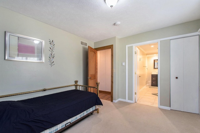 bedroom featuring a closet, visible vents, light carpet, a textured ceiling, and ensuite bath