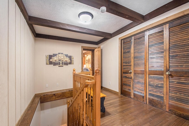 hall with a textured ceiling, an upstairs landing, baseboards, hardwood / wood-style floors, and beamed ceiling