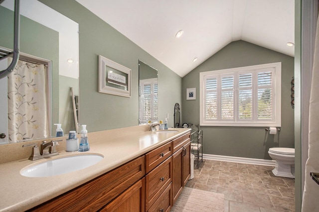 bathroom with double vanity, toilet, vaulted ceiling, a sink, and baseboards