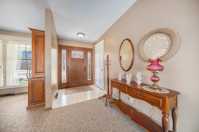 carpeted foyer featuring tile patterned flooring, visible vents, a textured ceiling, and baseboards