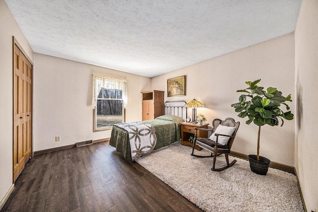 bedroom with dark wood finished floors, baseboards, visible vents, and a textured ceiling