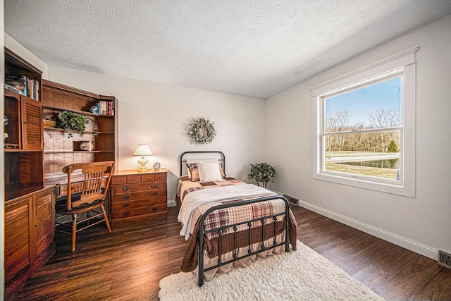 bedroom with visible vents, a textured ceiling, baseboards, and dark wood-style flooring