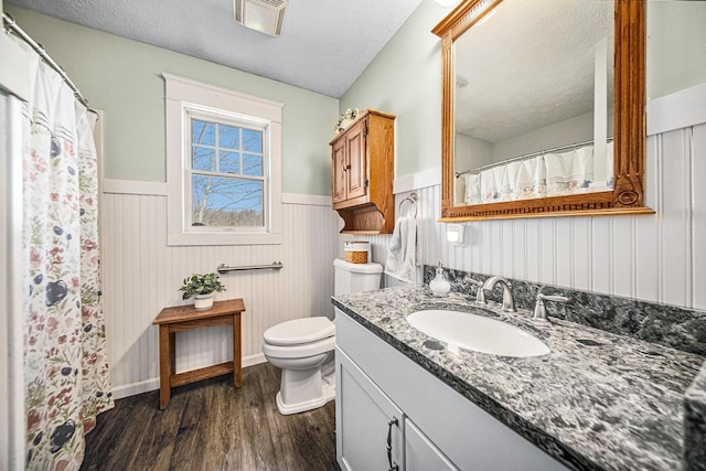 bathroom with toilet, vanity, wainscoting, wood finished floors, and a textured ceiling