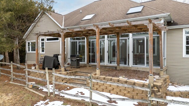 snow covered back of property featuring a pergola and a sunroom