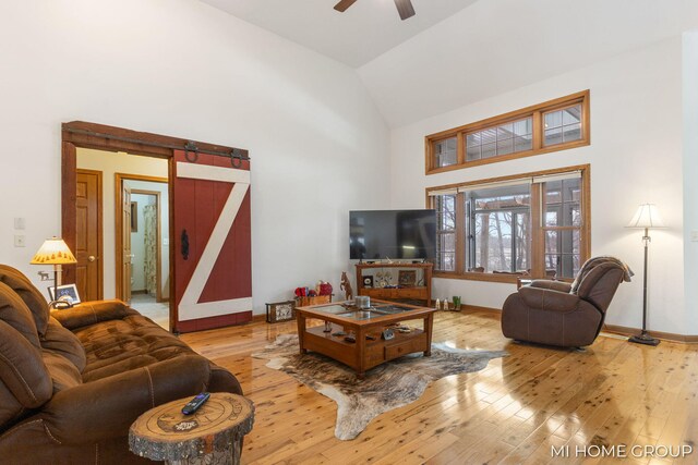 living room with ceiling fan, a barn door, high vaulted ceiling, and light wood-type flooring