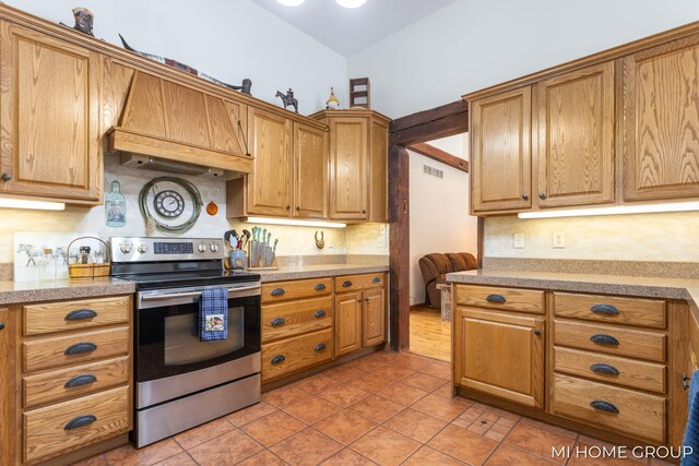 kitchen featuring stainless steel electric stove, custom range hood, and light tile patterned flooring