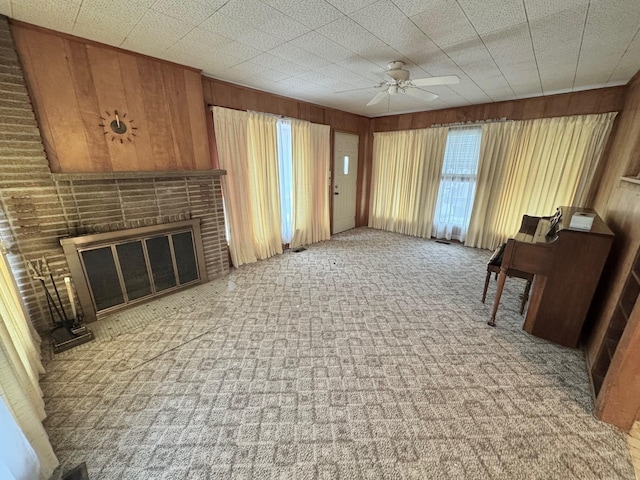 carpeted living room featuring ceiling fan, a fireplace, and wood walls