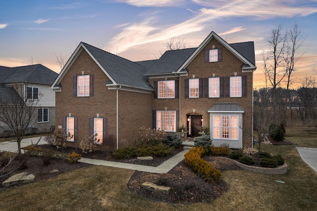 traditional-style house with roof with shingles, a front lawn, and brick siding