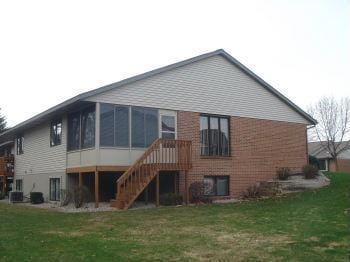 rear view of house with stairs, brick siding, a lawn, and a sunroom