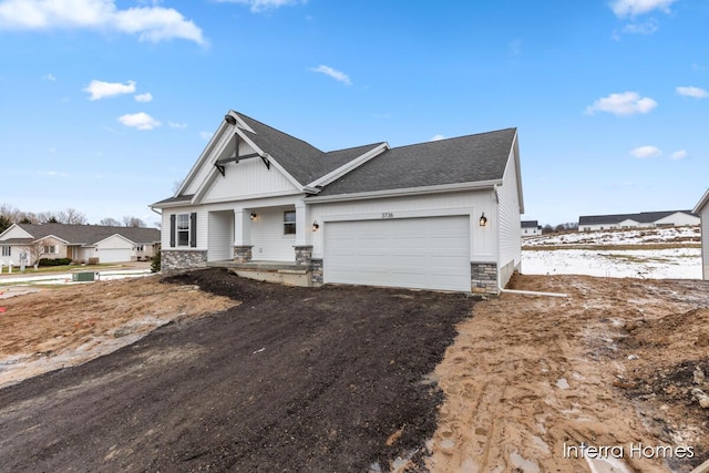 view of front of home featuring a garage, stone siding, roof with shingles, and driveway