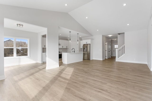 unfurnished living room featuring high vaulted ceiling, a healthy amount of sunlight, and light hardwood / wood-style floors