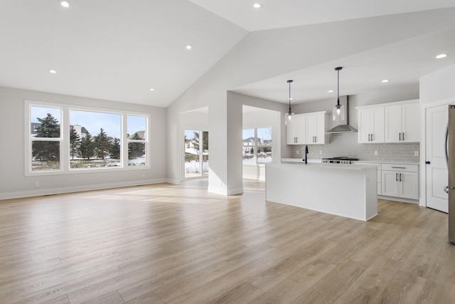 kitchen featuring white cabinetry, decorative light fixtures, light hardwood / wood-style flooring, a kitchen island with sink, and wall chimney range hood