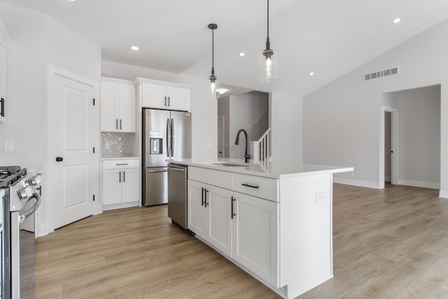 kitchen with sink, decorative light fixtures, an island with sink, stainless steel appliances, and white cabinets