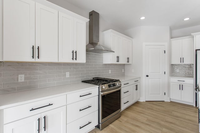 kitchen featuring white cabinets, wall chimney exhaust hood, light hardwood / wood-style flooring, and stainless steel gas stove