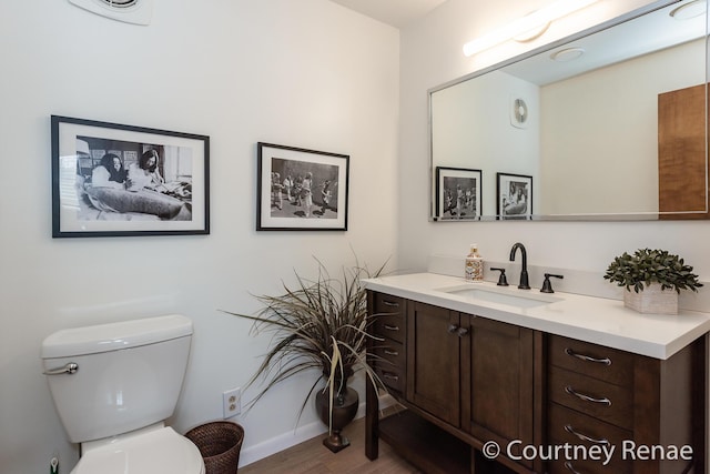 bathroom featuring baseboards, wood finished floors, toilet, and vanity