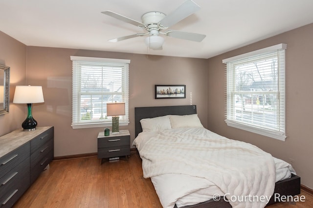 bedroom featuring ceiling fan, baseboards, wood finished floors, and multiple windows