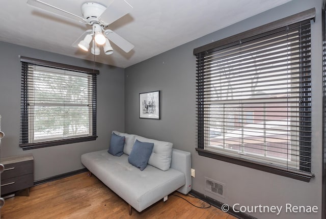living area with wood finished floors, visible vents, a ceiling fan, and baseboards