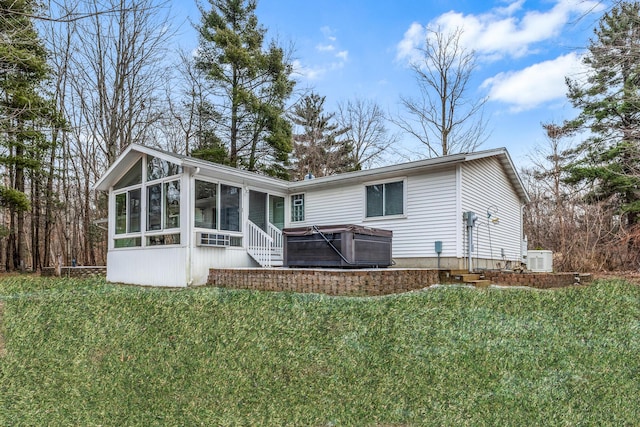 rear view of house featuring a hot tub, a sunroom, and a lawn