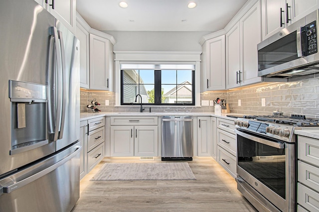 kitchen with light wood finished floors, stainless steel appliances, light countertops, backsplash, and a sink