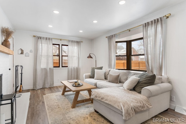 living room with light hardwood / wood-style floors, a brick fireplace, and a healthy amount of sunlight