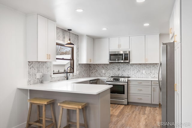 kitchen featuring a kitchen bar, sink, stainless steel appliances, kitchen peninsula, and hanging light fixtures