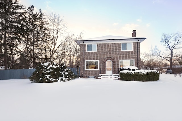 view of front facade with a chimney, fence, and brick siding