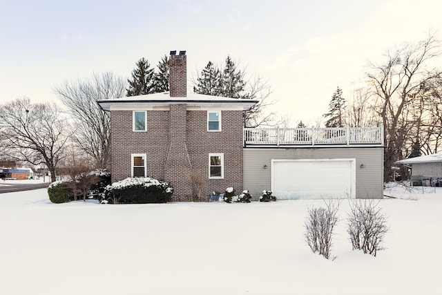 snow covered back of property featuring a garage, a chimney, and a balcony