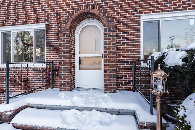 snow covered property entrance featuring a garage and brick siding