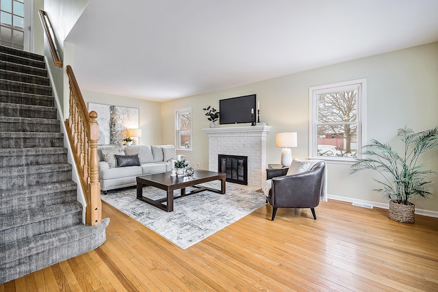 living area with a brick fireplace, stairway, and wood finished floors