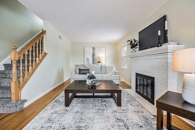 living room featuring a fireplace, visible vents, stairway, wood finished floors, and baseboards