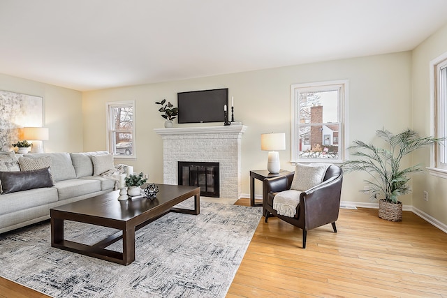 living area with light wood-type flooring, a brick fireplace, and baseboards