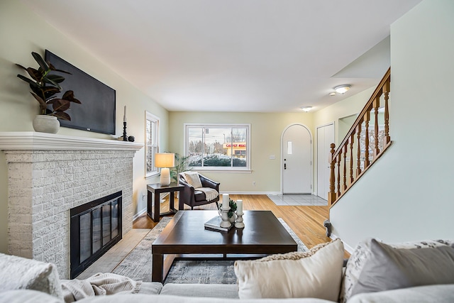 living area featuring light wood-type flooring, baseboards, a fireplace, and stairway