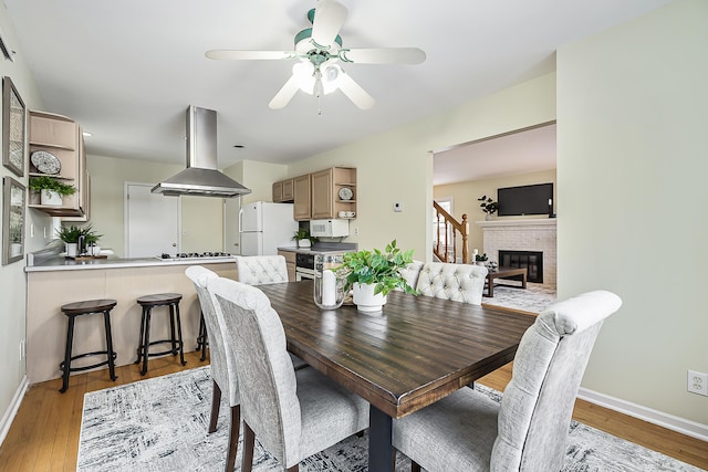 dining space featuring light wood-style flooring, a fireplace, baseboards, and a ceiling fan