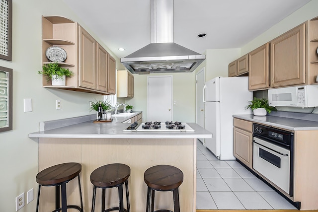 kitchen featuring open shelves, island range hood, white appliances, a peninsula, and a kitchen bar