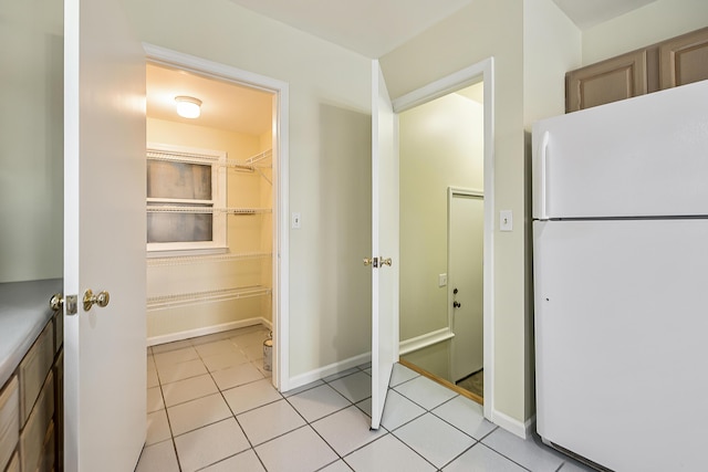 interior space featuring light tile patterned floors, freestanding refrigerator, and baseboards