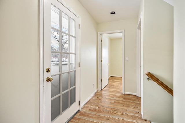 hall featuring light wood-style floors, an upstairs landing, and baseboards