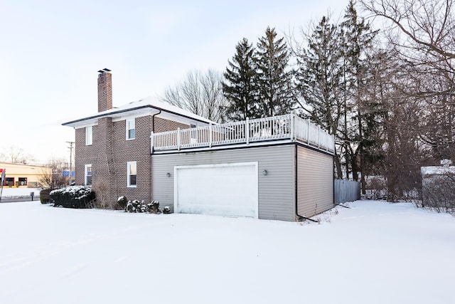 snow covered back of property featuring a garage, a chimney, and a balcony