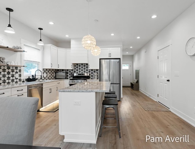 kitchen featuring sink, white cabinetry, decorative light fixtures, a center island, and stainless steel appliances