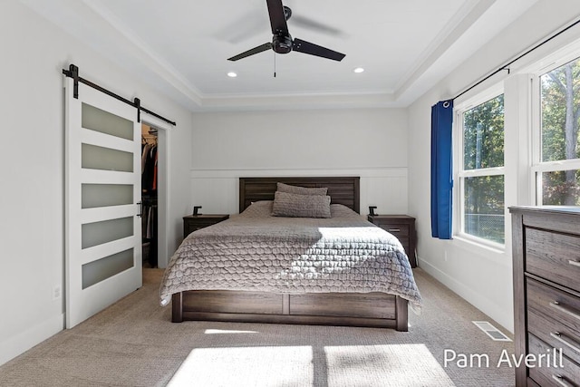 bedroom featuring a walk in closet, ceiling fan, crown molding, a barn door, and light carpet