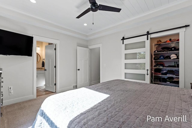 carpeted bedroom featuring ceiling fan, ensuite bath, a barn door, and a closet