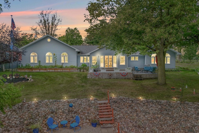 back house at dusk featuring a deck and a lawn