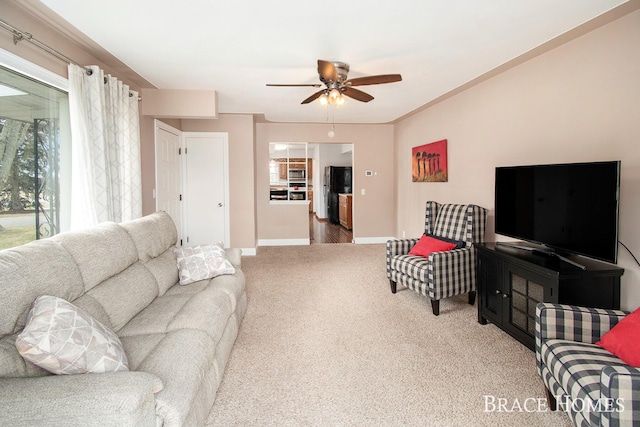 living area featuring carpet floors, ceiling fan, baseboards, and crown molding