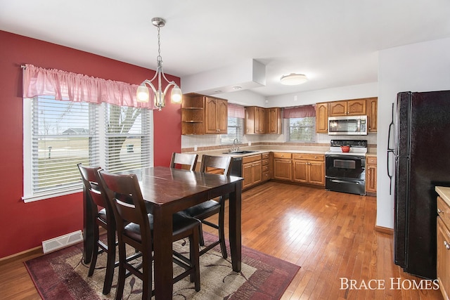 kitchen featuring visible vents, hardwood / wood-style flooring, black appliances, a chandelier, and a sink