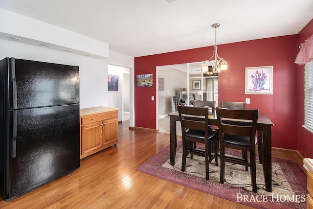 dining area with a chandelier, baseboards, and light wood finished floors