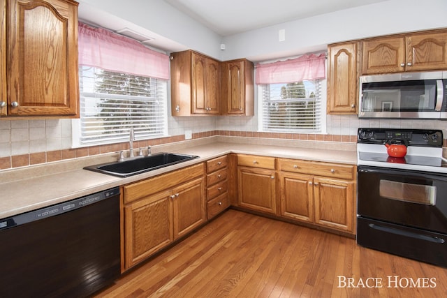 kitchen featuring tasteful backsplash, brown cabinetry, a sink, wood finished floors, and black appliances